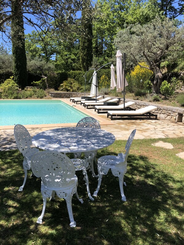 Ein Poolbereich mit Tisch und Stühlen, Liegestühlen und Sonnenschirmen.