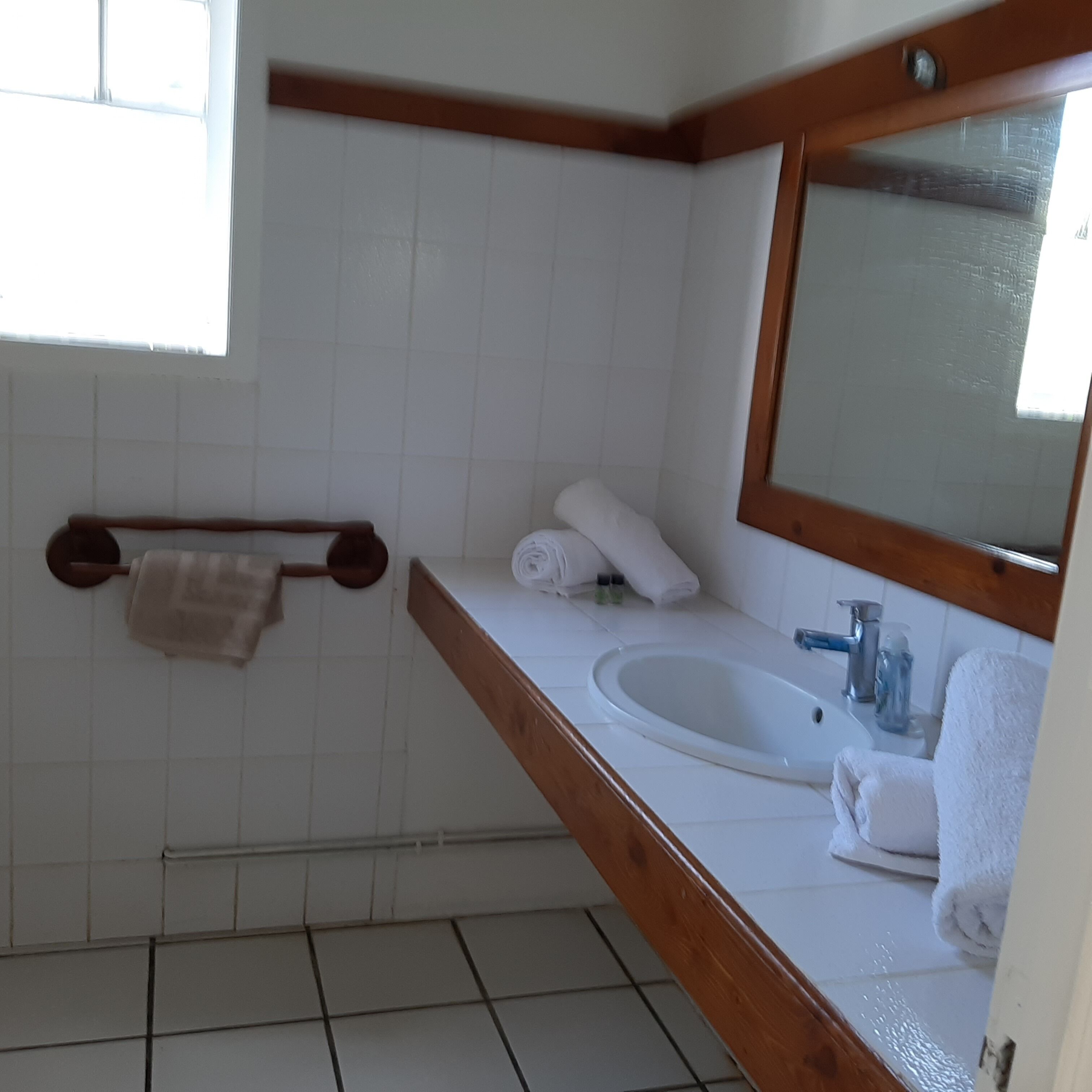 Un baño con lavamanos blanco, encimera de madera y un espejo. Hay toallas y artículos de aseo en la encimera.