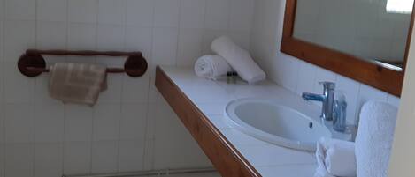 Un baño con lavamanos blanco, encimera de madera y un espejo. Hay toallas y artículos de aseo en la encimera.