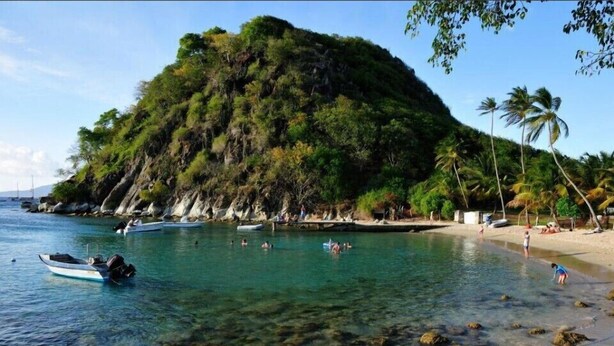 A beach with clear water, boats, and a rocky shoreline.