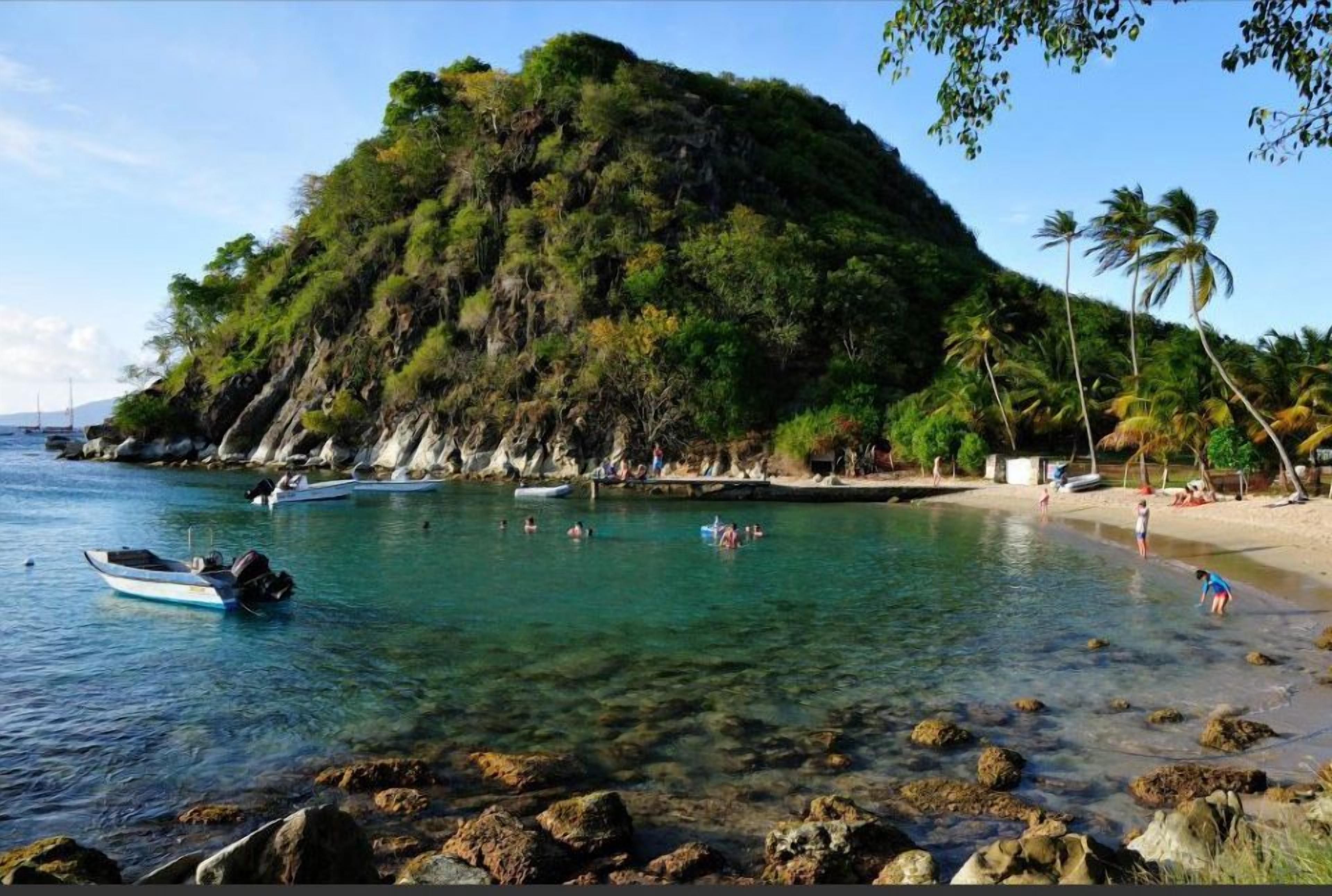 Una playa con agua cristalina, barcos y un litoral rocoso.