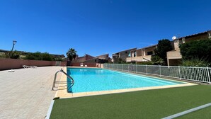 Ein Schwimmbecken unter blauem Himmel, umgeben von einem weißen Zaun und einem grünen Rasen.