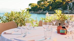 A table set for dining with wine glasses and bottles, overlooking a body of water and greenery.