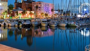 A marina with boats docked, a large building with a dome, and a Ferris wheel in the background.