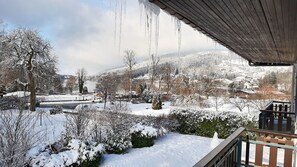 A snowy landscape with icicles hanging from a roof, a view of a town, and a snow-covered hill in the background. - Appart 100 m² Downtown in garden 2 Ha 300 m from the Lake (garden & lake views) (Gérardmer)
