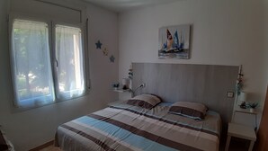 A bedroom with a bed, a window, a painting, and a nightstand. - Apartment with terrace close to shops and the beach (Ampuriabrava)