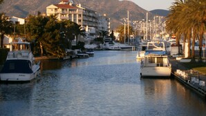 A marina with boats docked, a building with balconies, and mountains in the background. - Apartment with terrace close to shops and the beach (Ampuriabrava)