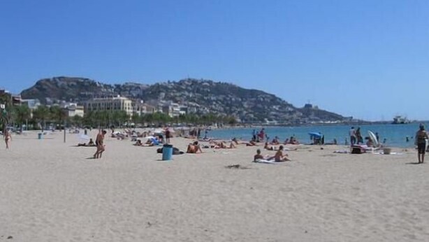 A beach with people sunbathing and swimming. There are buildings in the background and a hill. - Apartment with terrace close to shops and the beach (Ampuriabrava)