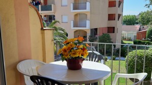 A balcony with a round table and chairs, a potted plant with yellow flowers, and a view of multi-story buildings in the background. - Apartment with terrace close to shops and the beach (Ampuriabrava)