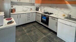Cocina compacta con alacenas blancas, estufa, horno y lavavajillas.