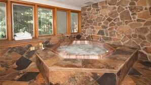 A stone-walled bathroom with a hot tub, large windows, and a bench with towels. - Ski In/Ski Out + Private Hot Tub + Sleeps 8 + Free Parking  (Keystone)