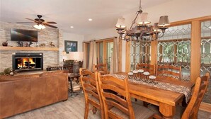 A dining area with a wooden table and chairs, a fireplace, and a television mounted on the wall. - Ski In/Ski Out + Private Hot Tub + Sleeps 8 + Free Parking  (Keystone)