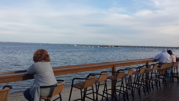 A wooden pier with wicker chairs facing a calm sea.