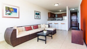 Un salon moderne avec un grand canapé d’angle, une table basse et une cuisine en arrière-plan.