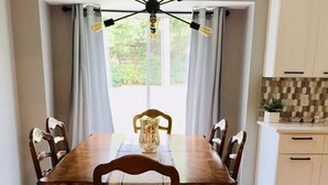 A dining room with a wooden table, six chairs, a chandelier, and a view of the outdoors through large windows. - Super close to campus and Lloyd Noble Center. Clean home with updated kitchen. (Norman)