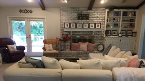 A living room with a white sectional sofa, a wicker chair, a fireplace with framed pictures, and a bookshelf. - Super close to campus and Lloyd Noble Center. Clean home with updated kitchen. (Norman)