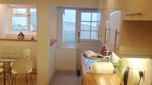 A compact kitchen with a dining area, a window, and a view of the street. -  Peaceful with Patio in Downalong, Moments from Beaches, Harbour, Town, Parking (St Ives)