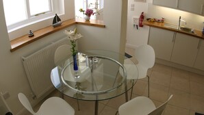 A modern kitchen with a glass dining table, white chairs, a wooden countertop, and a window with a view. -  Peaceful with Patio in Downalong, Moments from Beaches, Harbour, Town, Parking (St Ives)