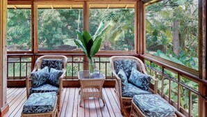 Une terrasse en bois, meublée de meubles en osier, et de grandes fenêtres donnant sur un jardin luxuriant.