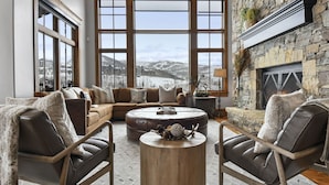 Una sala de estar acogedora con chimenea de piedra, ventanas amplias con vistas nevadas y asientos cómodos.