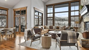Amplia sala de estar con un ventanal que ofrece vistas a un paisaje nevado, una chimenea acogedora y un comedor con muebles de madera.