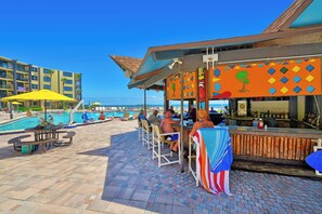 A poolside area with a bar and lounge chairs, overlooking a swimming pool and a building with balconies.
