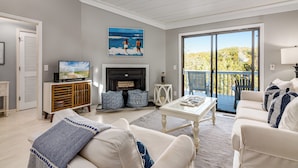 A living room with a fireplace, a television, and a balcony with a view of the outdoors. - Home Away From Home! 3 Bedroom Home Completely Updated; community pool access and BHI club access (Bald Head Island)