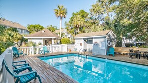 A swimming pool with a wooden deck and chairs, surrounded by palm trees and a small building with a sign. - Home Away From Home! 3 Bedroom Home Completely Updated; community pool access and BHI club access (Bald Head Island)
