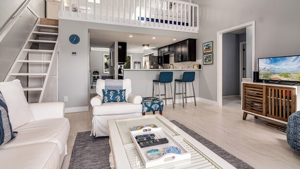 A spacious living area with a high ceiling, a staircase, a kitchen, and a dining area. - Home Away From Home! 3 Bedroom Home Completely Updated; community pool access and BHI club access (Bald Head Island)