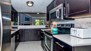 A modern kitchen with dark cabinets, stainless steel appliances, and a white countertop. - Home Away From Home! 3 Bedroom Home Completely Updated; community pool access and BHI club access (Bald Head Island)