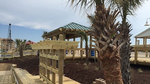 Een houten terras met een pergola, palmbomen en een blauwe ton in de achtergrond.