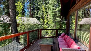 A wooden deck with a metal railing, a green table, and a pink sofa. - North Lake Tahoe, Mountain/Lake Views, Hot tub, Walk to Beaches, Vacation Rental (Tahoe Vista)