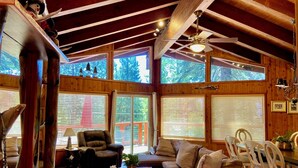 A cozy cabin interior with a wooden ceiling, large windows, a sofa, a chair, and a dining table. - North Lake Tahoe, Mountain/Lake Views, Hot tub, Walk to Beaches, Vacation Rental (Tahoe Vista)