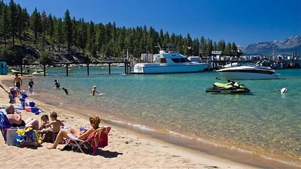 A beach with clear turquoise water, a dock with boats, and people relaxing on the sand. - North Lake Tahoe, Mountain/Lake Views, Hot tub, Walk to Beaches, Vacation Rental (Tahoe Vista)