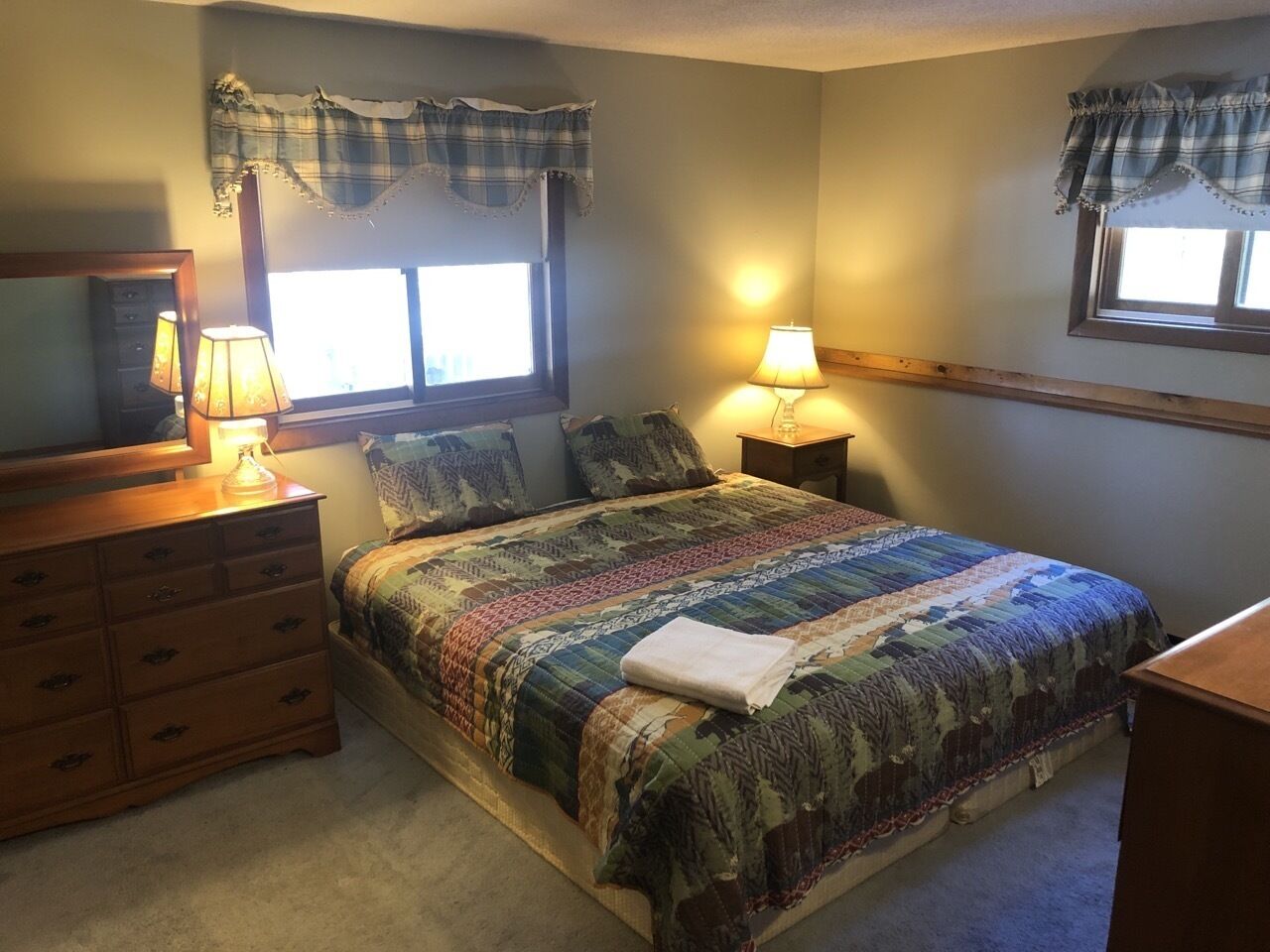 A bedroom with a bed, two bedside lamps, a dresser, and a window with curtains.