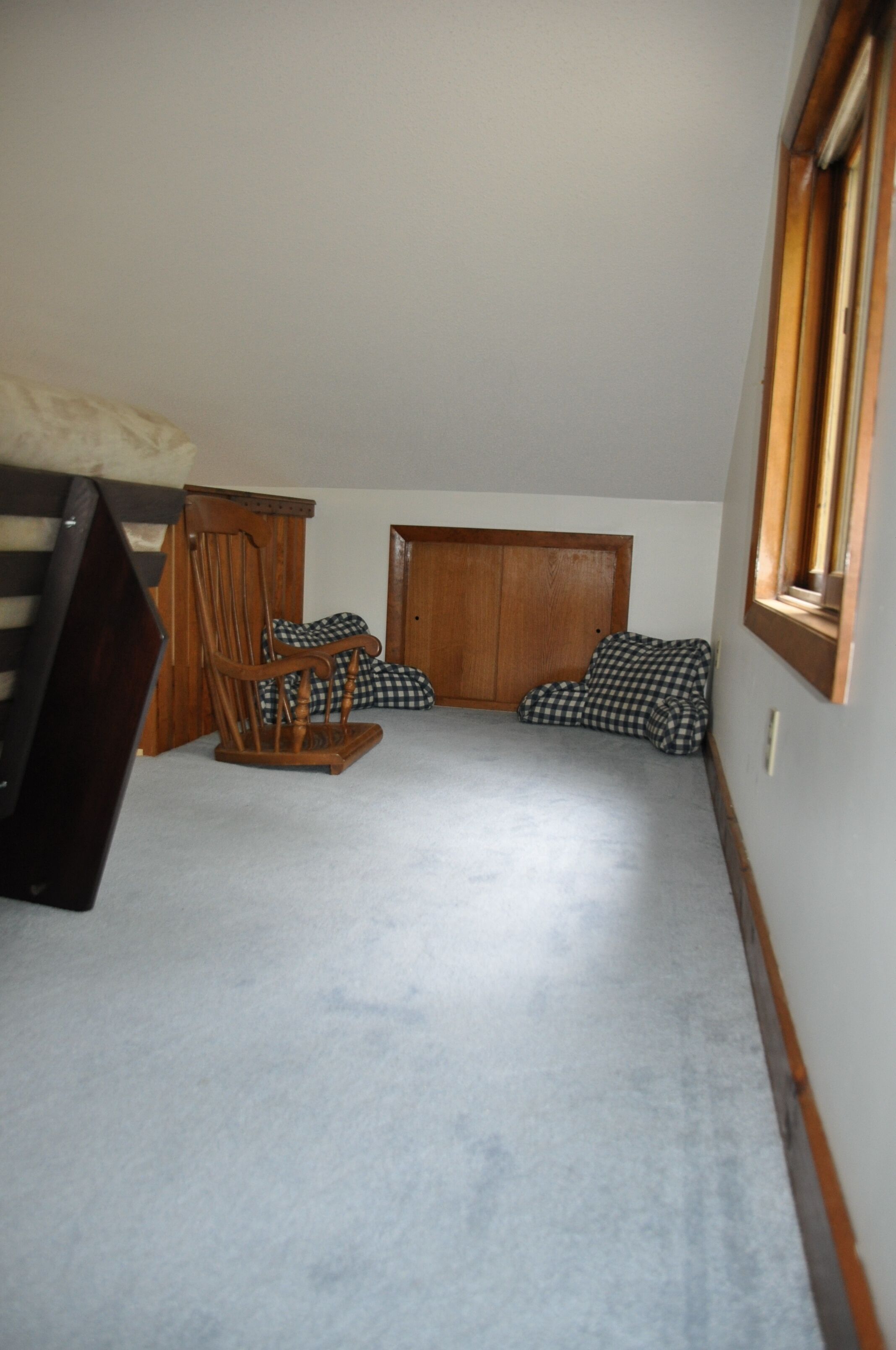 A room with a wooden rocking chair, a checkered sofa, and a wardrobe.