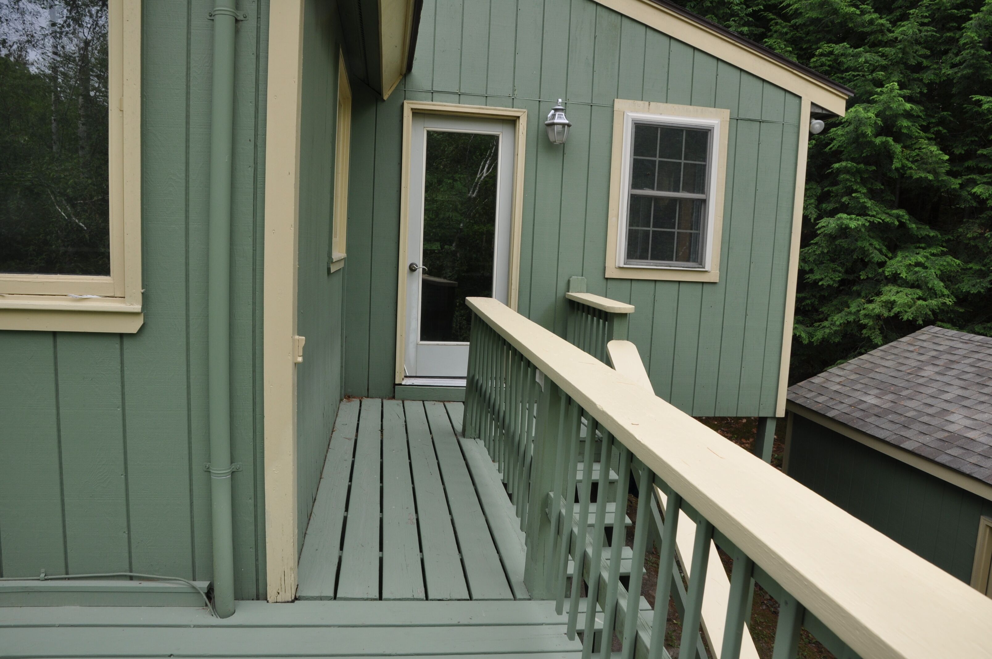A green wooden deck with a white railing, a door, and a window.
