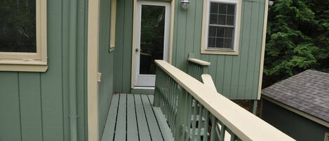A green wooden deck with a white railing, a door, and a window.