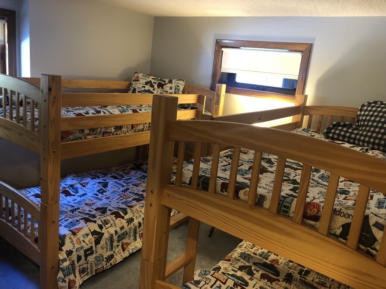 Une chambre avec un lit superposé, une fenêtre, des rampes en bois et une literie à motifs.