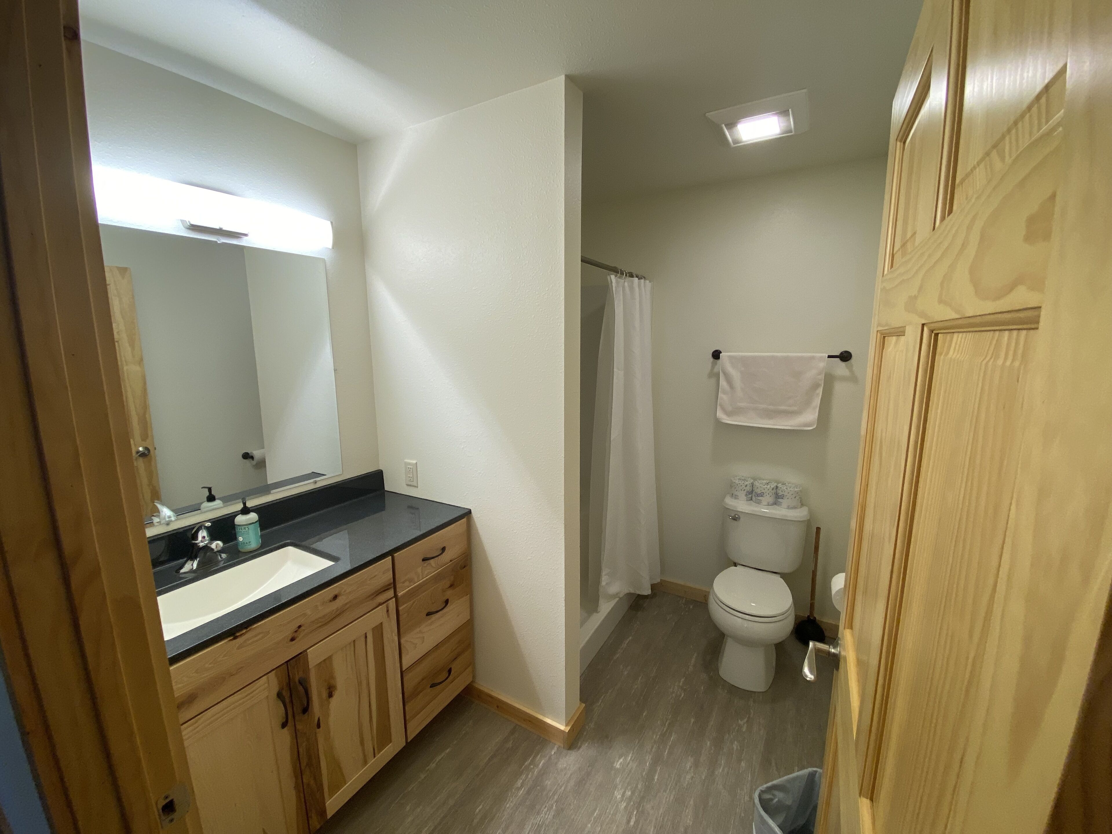 A bathroom with a wooden vanity, a toilet, and a shower curtain.