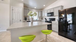 Une cuisine moderne avec des meubles blancs, un grand îlot central doté de tabourets, un réfrigérateur noir et un four à micro-ondes.