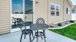 Une terrasse avec deux chaises en métal et une table ronde, une porte-fenêtre coulissante et un petit jardin avec des fleurs jaunes.