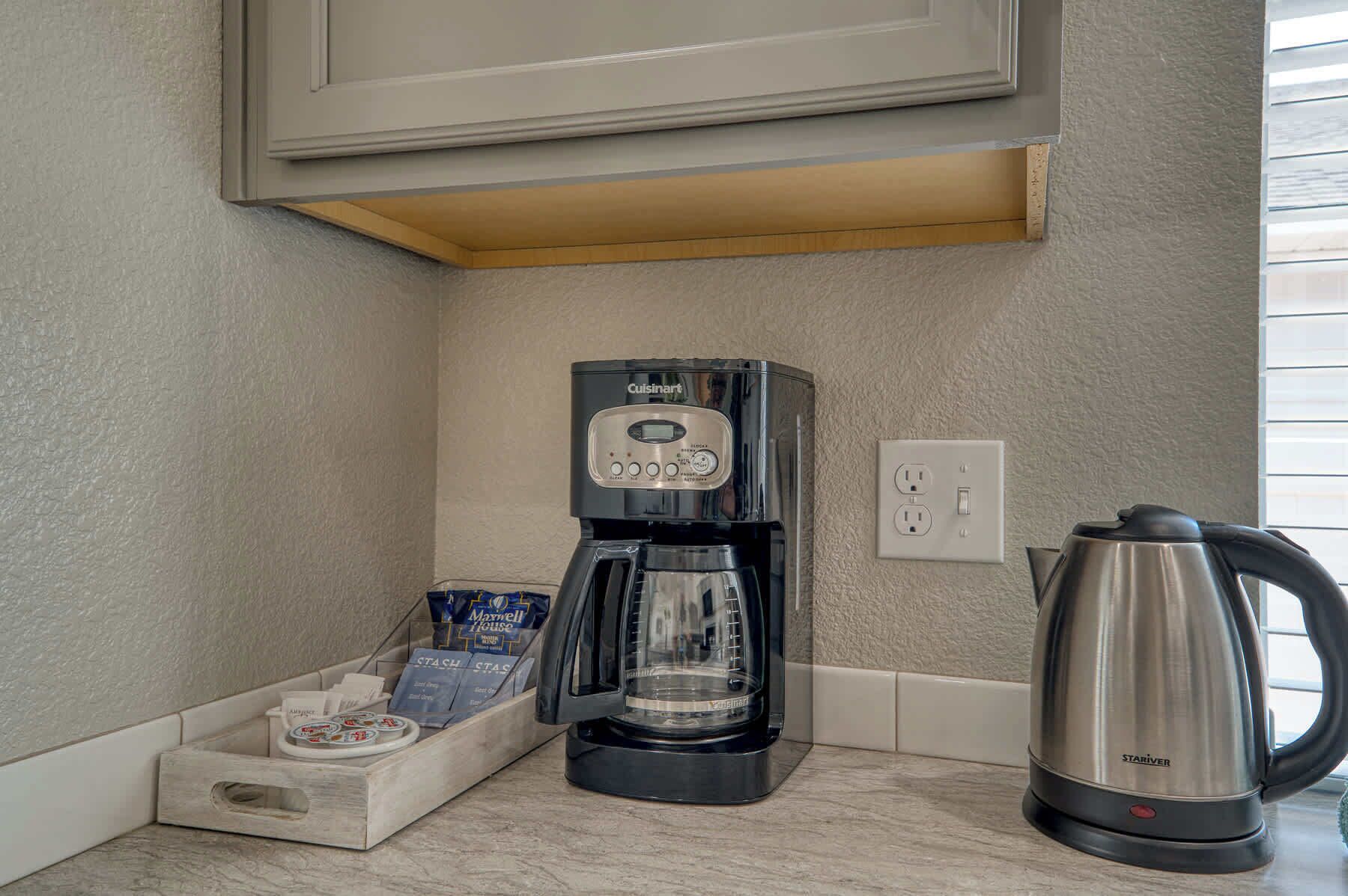 A kitchenette with a Cuisinart coffee maker, a Maxwell House coffee pod holder, a Starver kettle, and a white electrical outlet.