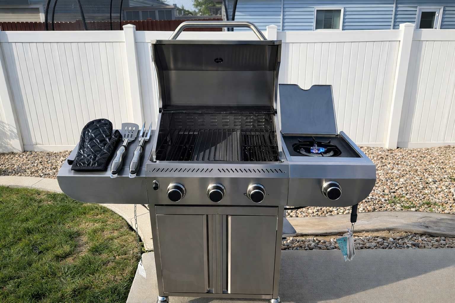 Ein Grill aus Edelstahl für den Außenbereich mit Seitenbrenner, integriertem Thermometer und einem Pfannenwenderhalter.