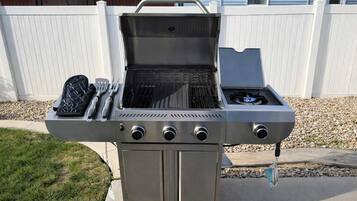 Ein Grill aus Edelstahl für den Außenbereich mit Seitenbrenner, integriertem Thermometer und einem Pfannenwenderhalter.