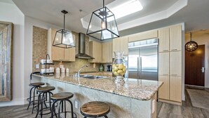 A modern kitchen with a central island, bar stools, and a large refrigerator. - PENTHOUSE DPH14:  3BR/3BA Sleeps 8 Amazing views and amenities (Orange Beach)