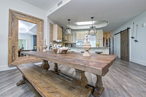 Uma cozinha ampla com uma mesa de madeira grande, luminárias pendentes e um espelho rústico.