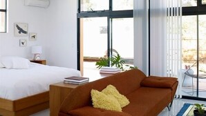A modern bedroom with a bed, a sofa, and a large window with blinds. - Featured in Sunset Magazine, Copper House is one of a kind (Tucson)