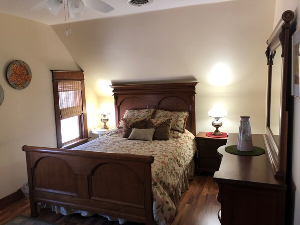 A bedroom with a wooden bed, a nightstand with a lamp, a mirror, and a window with blinds. - 1 BLOCK TO TOWN ~ 5 BLOCKS TO BEACH! Leave your car at home for the duration! (South Haven)