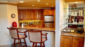 A kitchen with wooden cabinets, a granite countertop, a microwave, a refrigerator, and a glass display case with bottles. - LUXURIOUS AND SPACIOUS CONDO ,SKI IN/ SKI OUT IN BEAVER CREEK, COLORADO. (Avon)
